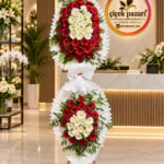 Fırfırlı beyaz çerçeveli iki katlı ferforje; kırmızı gerbera halkası içinde krem papatyalar