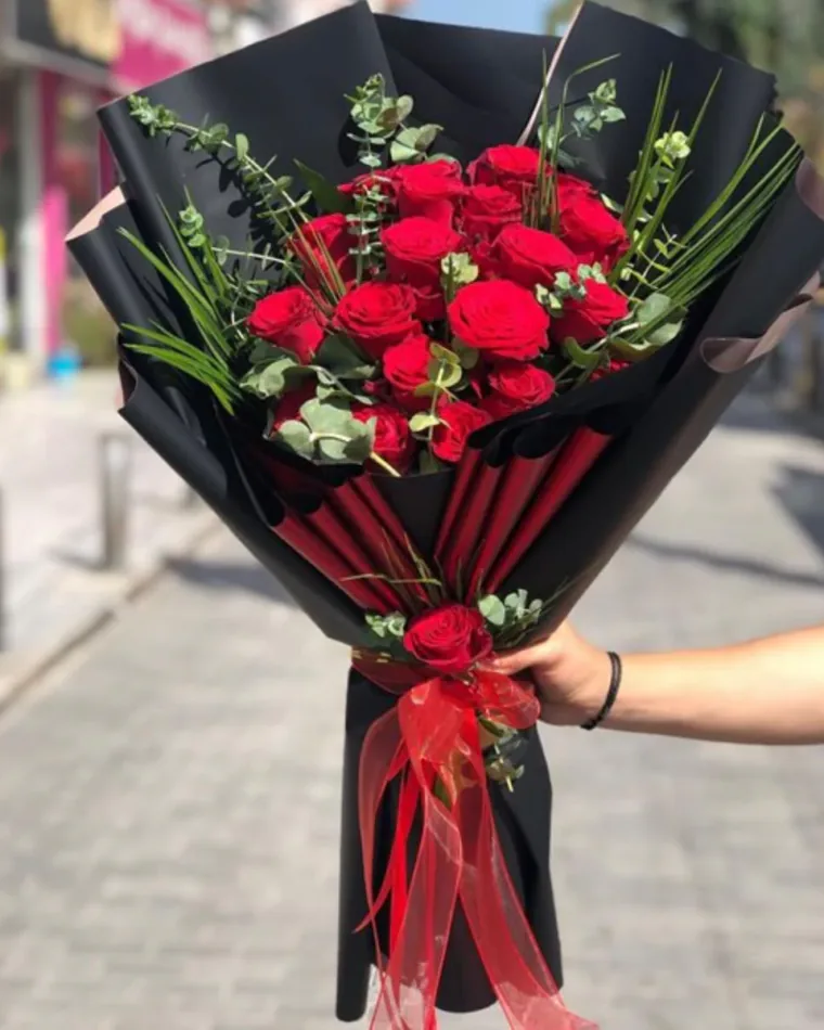 Siyah ambalajın içinden kırmızı pliseler görünen kırmızı gül buketi, organze kurdele ve tek gül