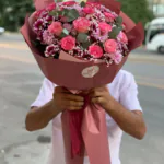 Buketin yakın planı; pembe güller, krizantemler ve ambalajdaki logo etiketi