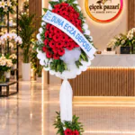 Tek katlı ferforje; dilimli beyaz panoda kırmızı gerberalar, kumaşla sarılı ayak ve dipte gerbera demeti