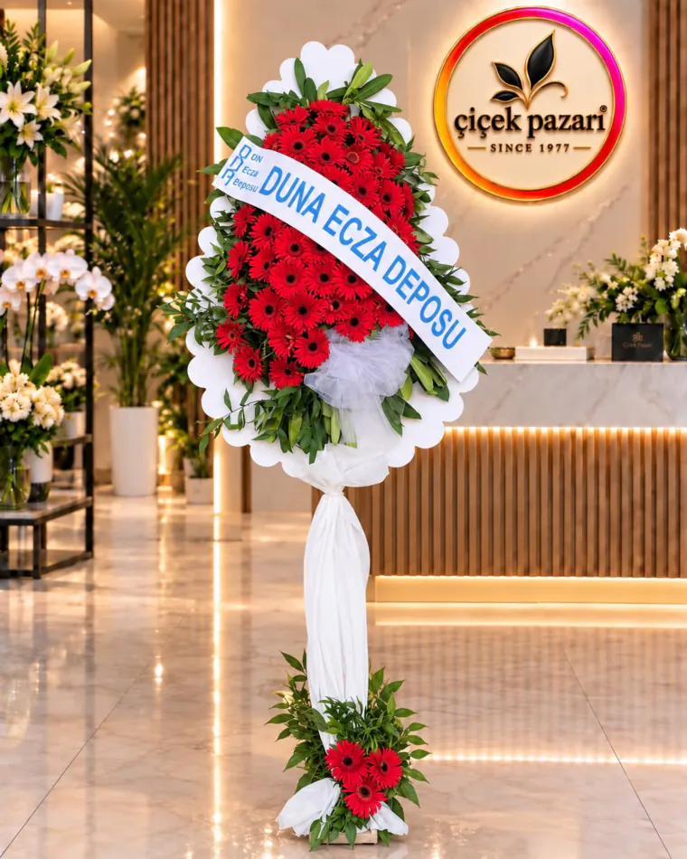 Tek katlı ferforje; dilimli beyaz panoda kırmızı gerberalar, kumaşla sarılı ayak ve dipte gerbera demeti